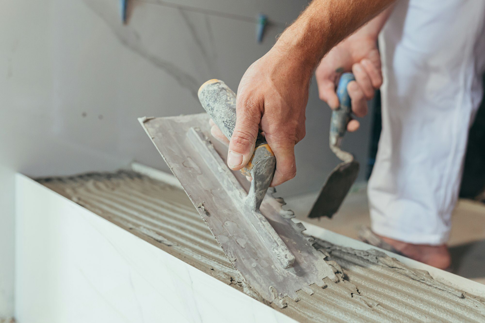 Male worker professional mounts ceramic tile in bathroom photo with close spatula with glue